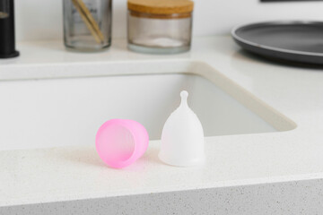 Fototapeta na wymiar Close-up of a pink and white menstrual cup on the edge of a bathroom sink. Concept of care during menstruation and reusable hygiene for women