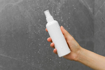 Female hand holding a white mockup jar of hair or skin care product under a stream of water in the...