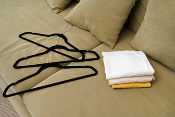 Neatly stacked clothes and black hangers on a green sofa. The concept of organizing space in an apartment, seasonal wardrobe replacement, tidying up and sorting