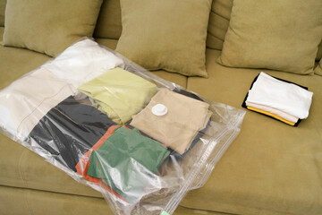 A transparent sealed bag filled with folded clothes lies on a green sofa. Concept of seasonal...