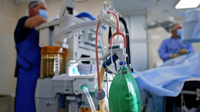Doctor's tools hanging on the apparatus. Stethoscope and ambu bag are on the modern lung ventilating machine. Surgeon works at backdrop in blur.