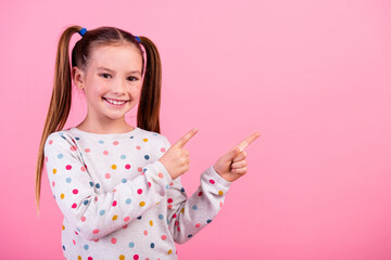 Portrait of cheerful schoolgirl with ponytails dressed dotted shirt indicating at discount empty...