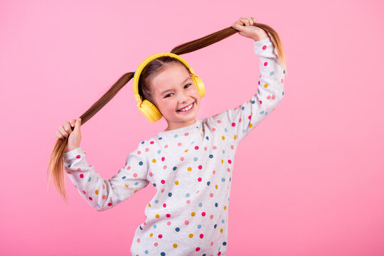 Portrait of cheerful schoolgirl with ponytails hairdo dressed dotted sleepwear in headphones hold tails isolated on pink color background