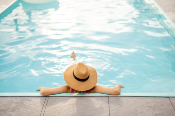 Woman in hat rests at swimming pool, view from a backside