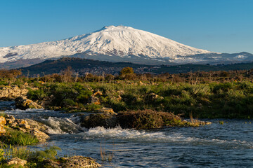 A seasonal river flows under the massive snowcovered Etna volcano. Favare Santa Venera  - obrazy, fototapety, plakaty