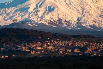 Bronte town under the snowy and majestic volcano Etna and a cloudy blue sky