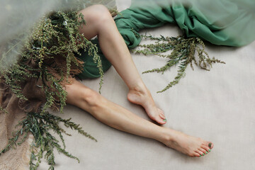 Women's legs with a green pedicure on a linen background with plants.