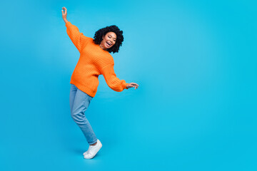 Full length photo of lovely young lady keep balance fall turn dressed stylish knitted orange garment isolated on blue color background