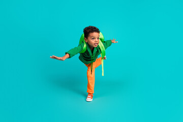 Full size photo of positive small boy with rucksack wear green hoodie hold arms like wings have fun...