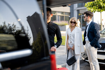 Business couple standing by a minivan taxi waiting for their chauffeur or porter to help them with a suitcases. Concept of business trips and travel