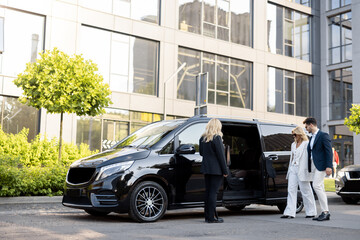 Female chauffeur waits a business people to let them in a minivan taxi, keeping door open. Concept of business trips and transportation service