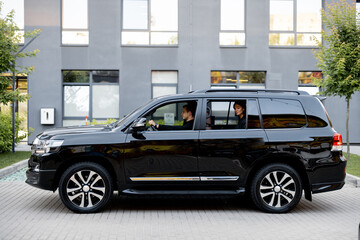 Side view of a luxury SUV vehicle with male driver and business lady on a backseat. Concept of...