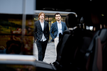 Two businessmen walk to the car from a building, view through a vehicle door. Concept of business transportation