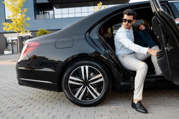 Portrait of elegant businessman gets out of a premium car. Transportation and business lifestyle...
