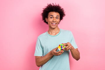 Photo of positive cheerful man dressed blue t-shirt playing rubic cube game isolated pink color...
