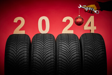 Winter car tires service and hand of mechanic with wrench and christmas ball, text 2024 happy new year on red background.