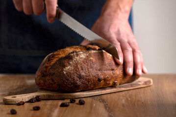 hands holding big homemade sourdough bread with seeds and cereals and bread knife cutting into slices - obrazy, fototapety, plakaty