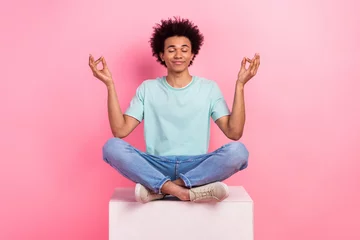  Full body photo of attractive young man sit podium meditate lotus pose wear trendy blue clothes isolated on pink color background © deagreez