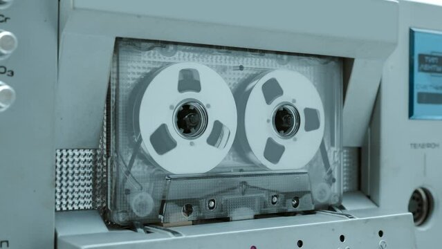 A cassette with shiny reels plays music in a Hi-Fi recorder from 80s of silver  color. Closeup. Shot in motion