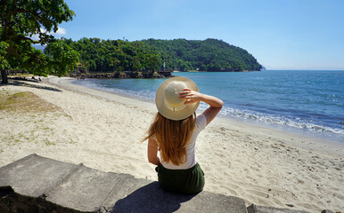 Holidays in Brazil. Back view of traveler girl sitting on wall in Ubatuba beach, Brazil.