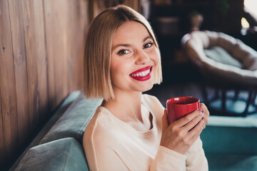 Profile portrait of stunning positive person beaming smile sit comfy couch hold coffee mug loft interior flat inside