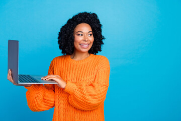 Photo portrait of attractive young woman hold laptop look empty space wear trendy knitwear orange clothes isolated on blue color background