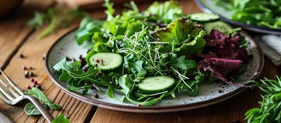 Deurstickers Plate with a healthy salad of greens, cucumber, and avocado. © TheWaterMeloonProjec