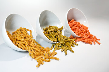 Three white bowls with different legume pasta fusilli made from chickpeas, mung beans and red...