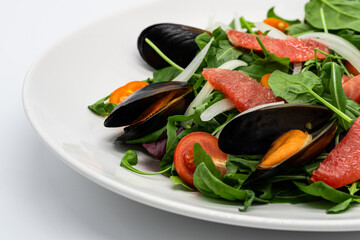 Salad with spinach, tomatoes, mussels and grapefruit on the white plate 