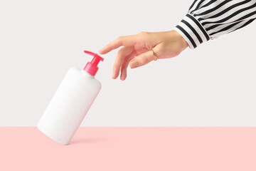 Womans hand touch white bottle on pastel pink and white background. Self care concept