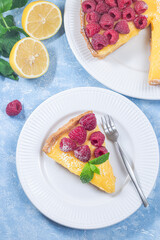 Piece of delicious lemon tart with fresh raspberry, on plate, vertical top view, closeup
