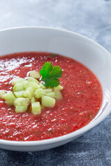 Soup Gazpacho garnished with cucumber and cilantro, in white bowl, vertical closeup