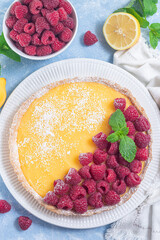 Lemon tart, garnished with fresh raspberry, icing sugar, mint, on white plate, vertical top view