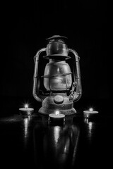 Horizontal black and white Image of an antique lantern, light painted with four votive candles surrounding it.  
