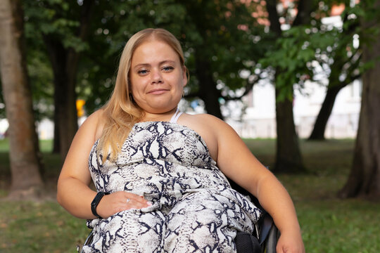 Smiling Brightly Young Woman With Short Stature Sitting In Wheel Chair In Green Park Outdoor. October Dwarfism Awareness Month. Horizontal
