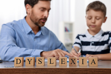 Father helping son with homework and cubes with word Dyslexia at table indoors, selective focus - obrazy, fototapety, plakaty