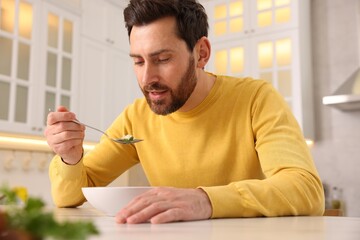 Man eating delicious chicken soup at light table in kitchen