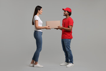 Smiling courier giving parcel to receiver on grey background