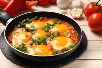 Delicious shakshuka in frying pan on light wooden table, closeup
