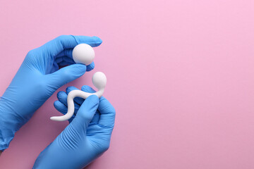 Reproductive medicine. Fertility specialist in gloves holding figures of sperm and egg cells on pink background, top view with space for text