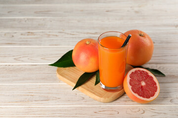 Tasty grapefruit juice in glass and fresh fruits on light wooden table. Space for text