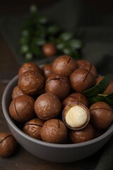 Tasty Macadamia nuts and green twig in bowl on wooden table, closeup