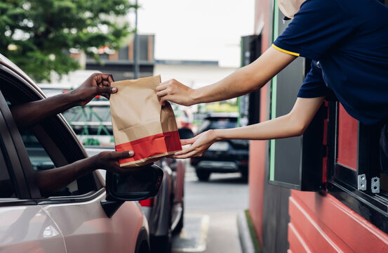 Hand Man in car receiving coffee in drive thru fast food restaurant. Staff serving takeaway order for driver in delivery window. Drive through and takeaway for buy fast food for protect covid19.