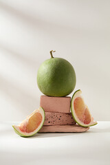 Front view of pink pomelo and pomelo slices displayed on pink blocks of stone on white background....