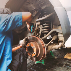 Car mechanic hands replace brakes in garage. Worker changing brake disc in auto repair workshop. - obrazy, fototapety, plakaty