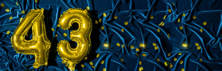 number forty three, gold foil balloon number on a blue velvet background with confetti. Birthday...