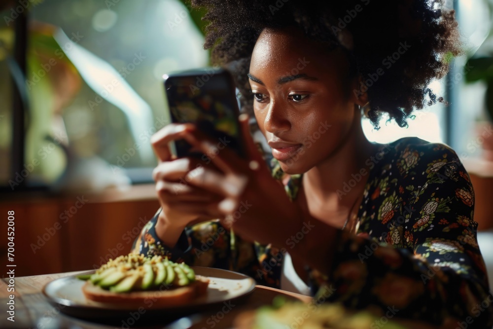 Poster a woman sitting at a table, focused on her phone while a plate of food sits in front of her. this im