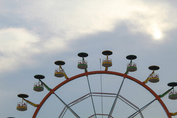 Ferris wheel with sun and cloudy blue sky background