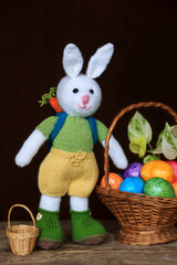 Knitted white rabbit with a rucksack standing with a basket of Easter eggs