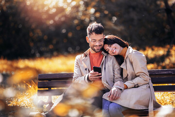 Young couple looking reading messages on smart phone in park